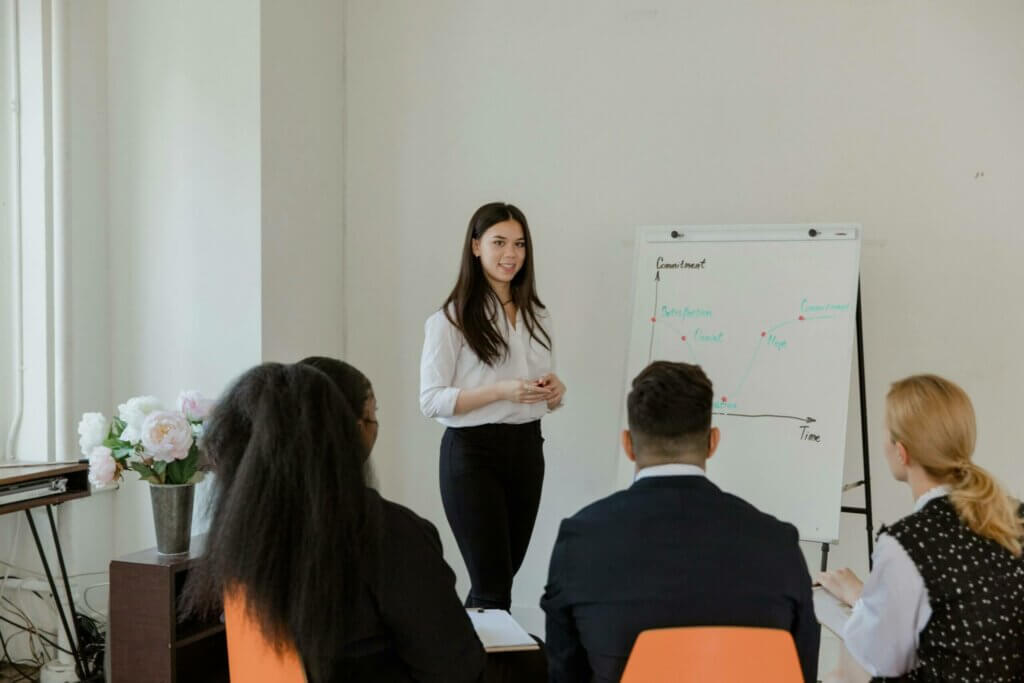 Femme leader - coaching collectif en leadership Femme leader animant une session de coaching collectif en leadership féminin devant tableau blanc, avec équipe mixte attentive, illustrant coaching d'équipe et intelligence collective.