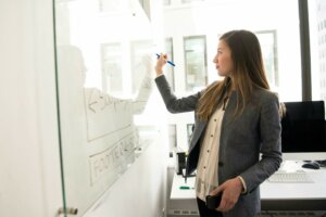 coaching femmes leader Femme manager confiante écrivant au tableau blanc lors d'une séance de coaching leadership, illustrant posture managériale et développement professionnel des femmes leaders.