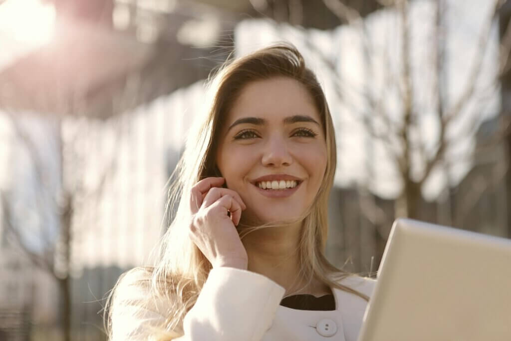 Le leadership féminin en entreprise Jeune femme dirigeante souriante au téléphone avec tablette numérique, en extérieur devant un bâtiment moderne, symbolisant le leadership féminin confiant et la connectivité professionnelle.