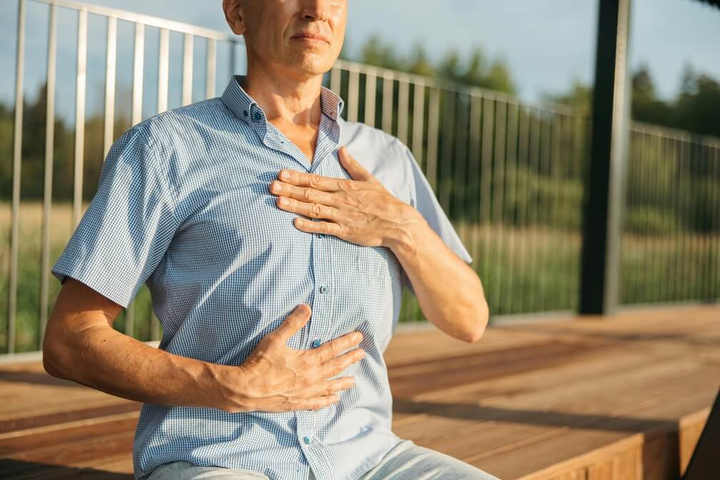 sophrologie-respiration-abdominale Un homme assis qui pratique une respiration abdominale profonde typique de la sophrologie : mains posées sur le ventre, posture détendue, yeux clos, pour mieux sentir le diaphragme et activer le nerf vague, comme je vous l'enseigne en séance à Vincennes.